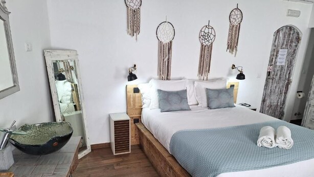 Um quarto com cama de madeira, abajures, um espelho, uma tigela sobre uma mesa e sonhadores pendurados na parede.