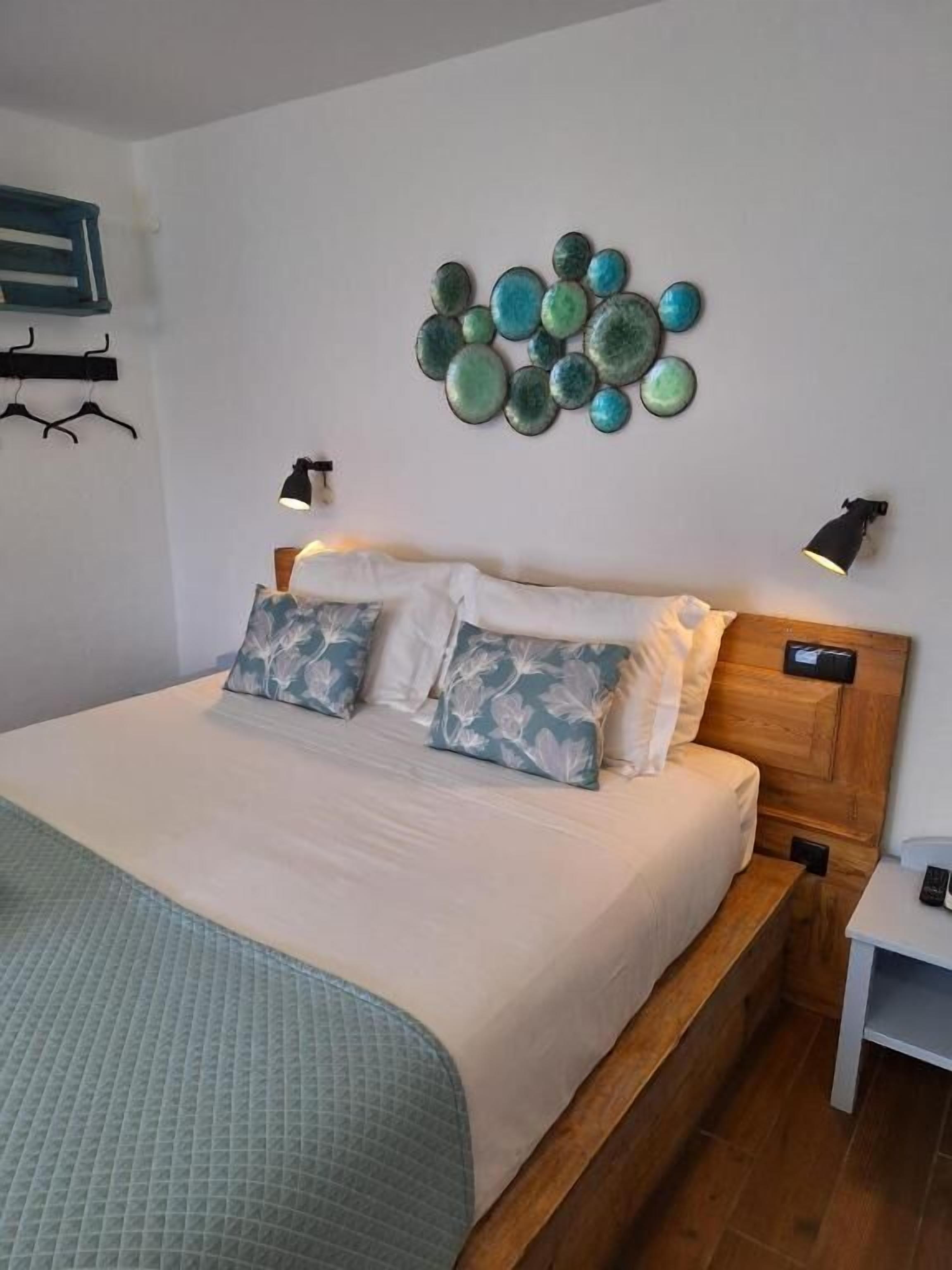 A neatly made bed with a quilted bedspread, two pillows with a leaf pattern, and a wall-mounted light fixture.