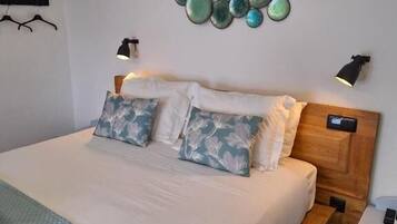 Una cama bien tendida con una colcha acolchada, dos almohadas con diseño de hojas y una lámpara de pared.