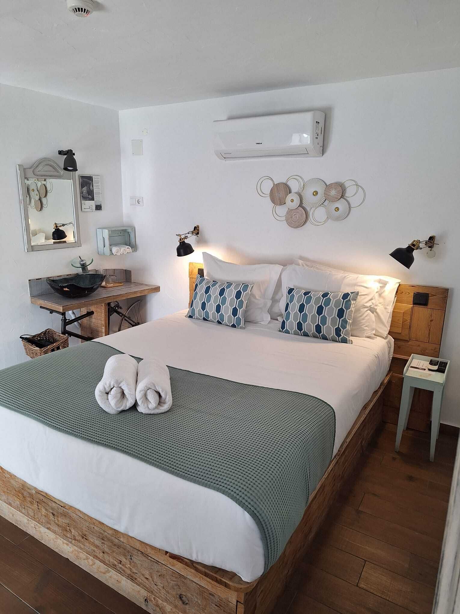 Un dormitorio con una cama grande, una mesita de noche, un espejo, un aire acondicionado de pared y un adorno en la pared.