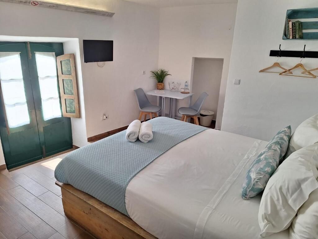 A bedroom with a bed, a desk, two chairs, a small table, a TV, and a door.