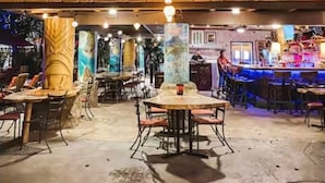 Ein Restaurantbereich im Freien mit Tischen und Stühlen, eine Bar mit Theke und dekorative Hängelampen.