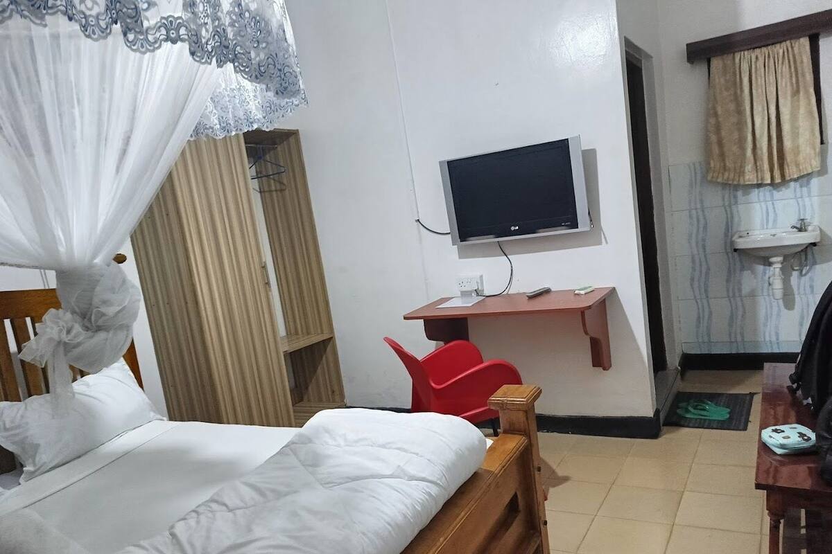 Ein Hotelzimmer mit einem Bett, einem Schreibtisch mit Stuhl, einem Fernseher und einem Badezimmer mit Waschbecken.