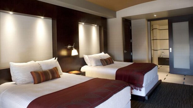 Habitación de hotel con dos camas, cabecera de madera oscura, lámparas de noche y un espejo grande.