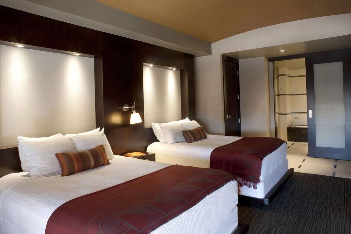 Ein Hotelzimmer mit zwei Betten, einem dunklen Holz-Kopfteil, Nachttischlampen und einem großen Spiegel.