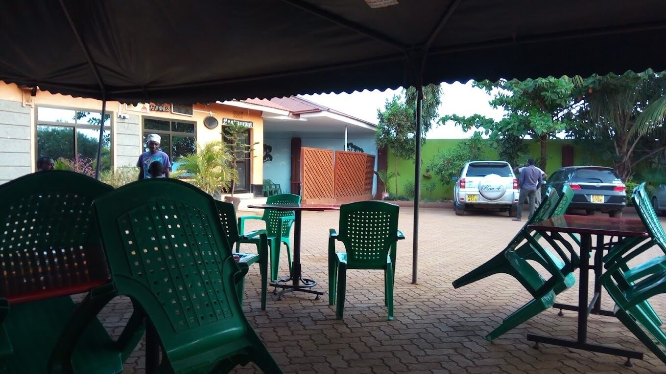An outdoor seating area with green plastic chairs and tables, a covered section with a roof, and a building with a 'Guinness' sign in the background.