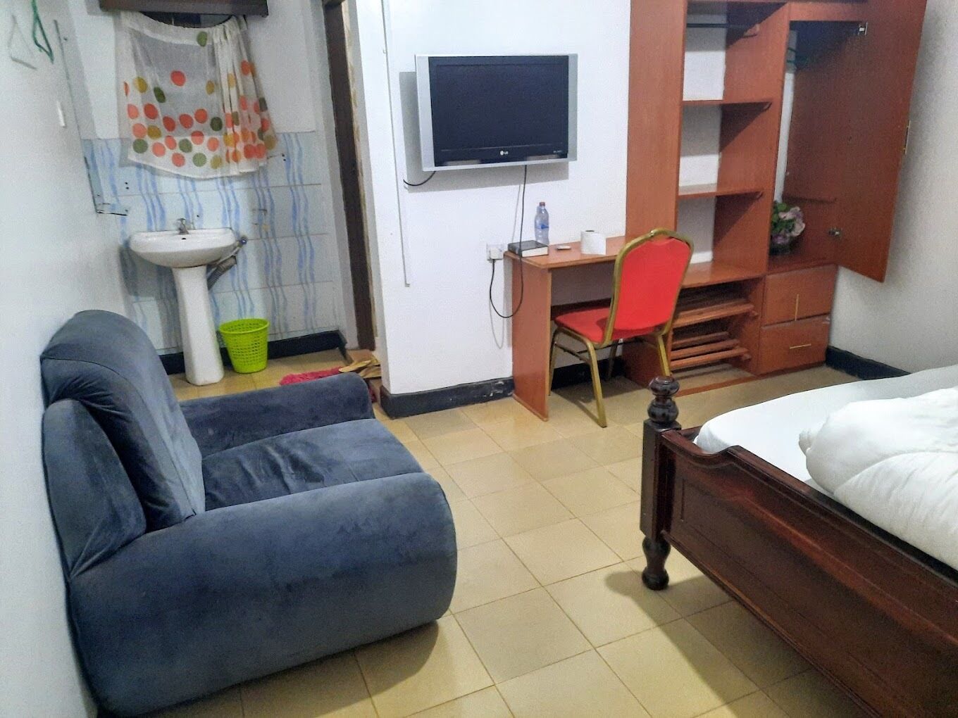 Une pièce comprenant un lit, un bureau avec une chaise, une télévision, un lavabo et une fenêtre avec des rideaux.