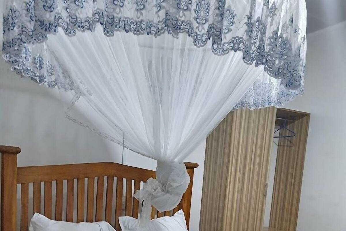 Ein ordentlich bezogenes Bett mit weißen Leinen und Kissen, ein hölzernes Kopfteil und ein Baldachin mit Spitzenbesatz.