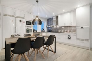 A modern kitchen with white cabinetry, a wooden dining table, and black chairs.