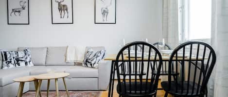 A modern living room with a grey sofa, black chairs, a round wooden table, and three framed animal prints on the wall.