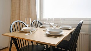 A dining table set with white plates, bowls, and wine glasses, surrounded by black chairs, in a room with a window and curtains. - Cozy Studio, Free Parking By Lapland Host (Rovaniemi)