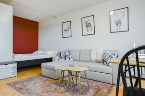 A modern living room with a sofa, a small round table, a bed, and a red accent wall.