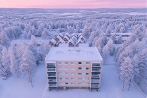 A multi-story building with a flat roof, surrounded by snow-covered trees. - Cozy Studio, Free Parking By Lapland Host (Rovaniemi)