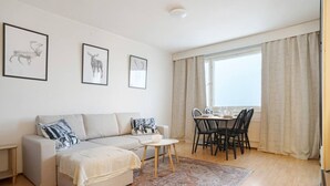 A modern living room with a sofa, a dining table with chairs, and a large window with curtains. - Cozy Studio, Free Parking By Lapland Host (Rovaniemi)