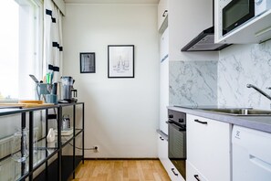 A modern kitchen with white cabinets, a marble backsplash, a stainless steel sink, and a microwave. There are two framed pictures on the wall.
