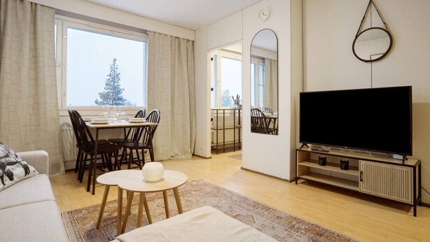 A modern living room with a sofa, a dining table set for four, a TV, and a large window with curtains. - Cozy Studio, Free Parking By Lapland Host (Rovaniemi)