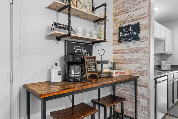 A kitchen counter with a coffee maker, mugs, and a chalkboard sign. - Ashley's Charming Chalet (Branson)