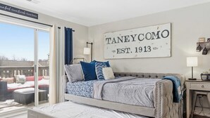 Ein Schlafzimmer mit einem großen Bett, Blick ins Freie, einem Schild an der Wand und einem kleinen Tisch mit einer Lampe.