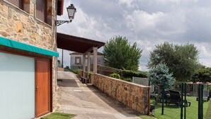 Ein Steinhaus mit Garage, einem gepflasterten Weg und einem umzäunten Bereich mit Grünflächen.