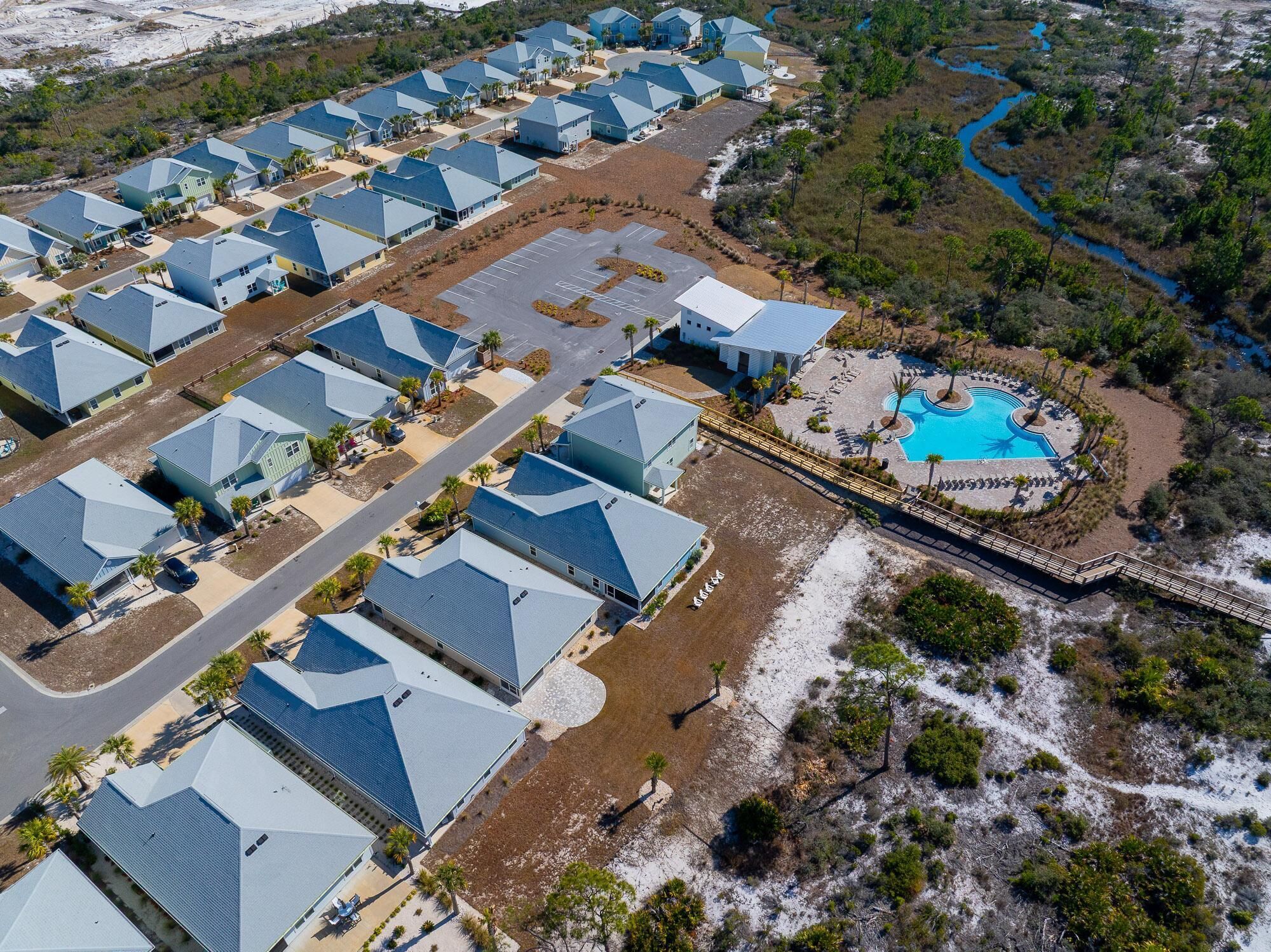 An aerial view of a resort with multiple blue-roofed buildings arranged in rows, a central swimming pool, and a surrounding natural landscape.