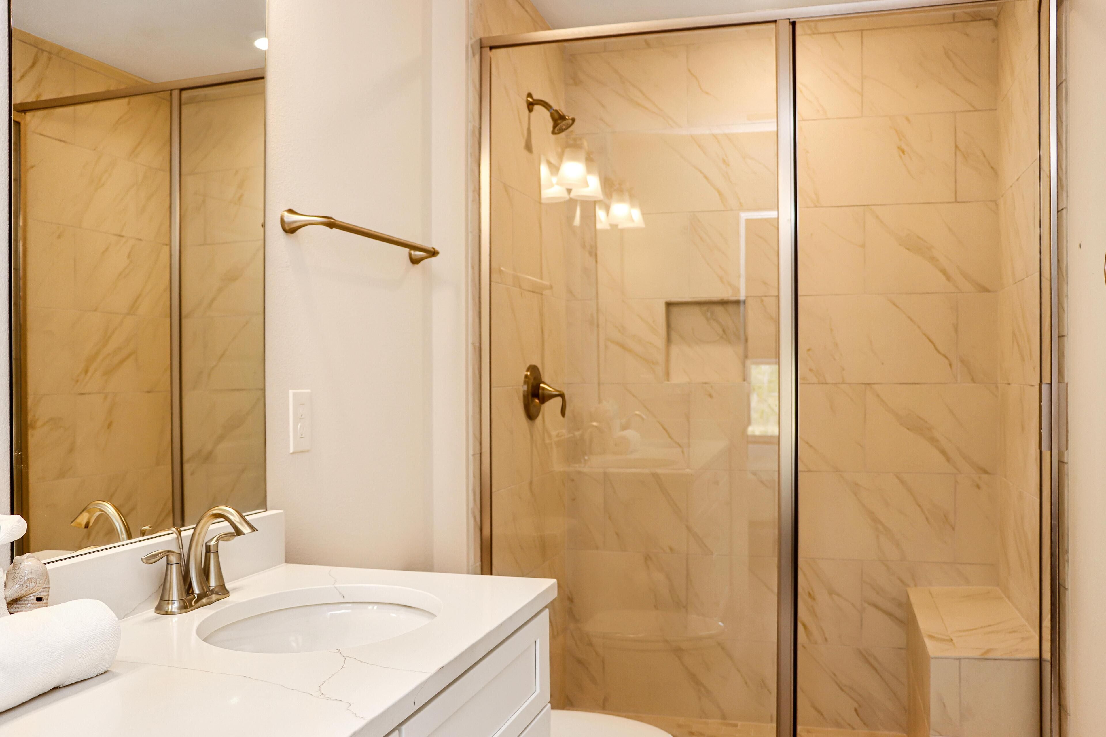 A modern bathroom with a large mirror, two sinks, a shower with a glass door, and a toilet.