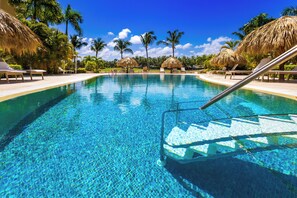 A clear swimming pool with lounge chairs and thatched umbrellas. - Iberostate 2 BR Lake & Golf View Condo (Punta Cana)