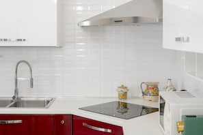 Cozinha com armários brancos, pia de aço inoxidável, micro-ondas e fogão.