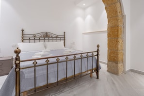Quarto com cama, cabeceira de madeira, coluna de pedra e mesa de cabeceira.