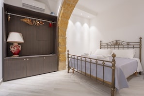 A bedroom with a bed, a wardrobe, a lamp, and a stone wall. - Ortigia Inner Suites | Piazza Archimede and the Cathedral, 2 bedrooms and 2 bathrooms (Siracusa)