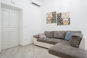 A living room with a grey sofa, a white door, and two wall-mounted artworks. - Ortigia Inner Suites | Piazza Archimede and the Cathedral, 2 bedrooms and 2 bathrooms (Siracusa)
