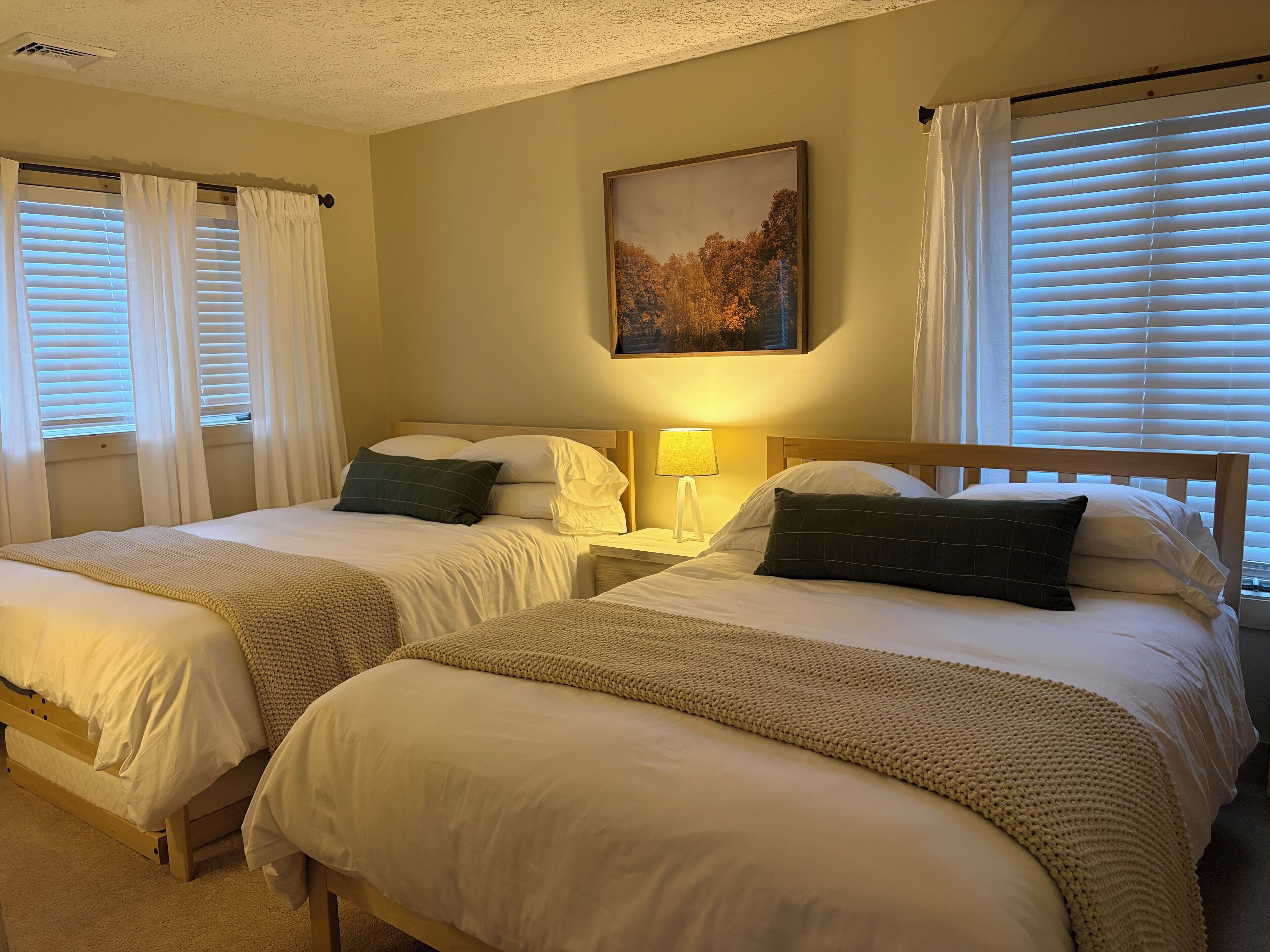 A hotel room with two single beds, a nightstand with a lamp, and a painting on the wall.