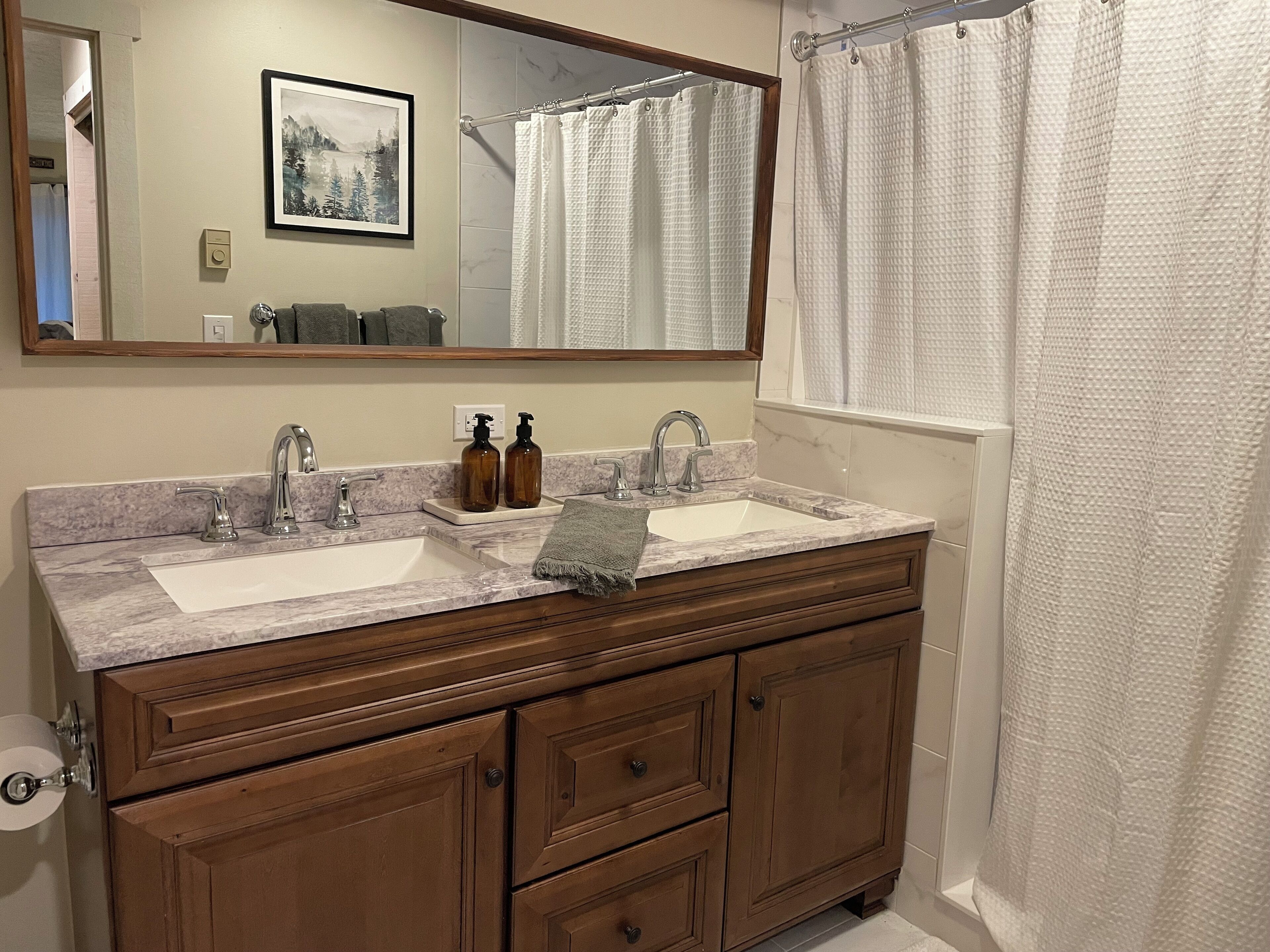 A bathroom with two sinks, a large mirror, wooden cabinets, and a shower curtain.