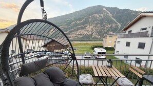 Un balcón con una silla colgante, una mesita y vistas a un estacionamiento y edificios al fondo.