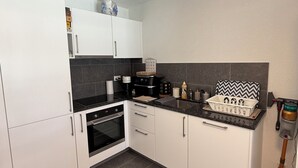Una cocina compacta con armarios blancos, encimera negra y salpicadero de azulejos.