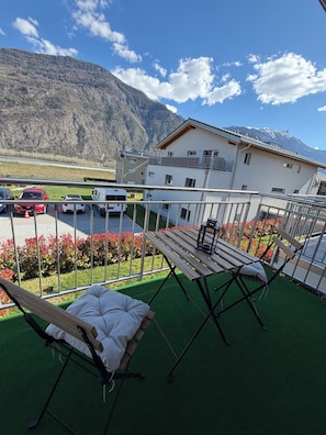 A balcony with a view of a mountain, a parking area with cars, and a building with a balcony. - Cosy Valais 80m² Mountain View Apartment (Chamoson)
