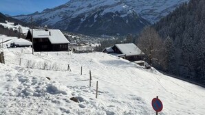 Paisaje nevado con una cadena montañosa al fondo, una cabaña de madera y un cartel de prohibido estacionar.