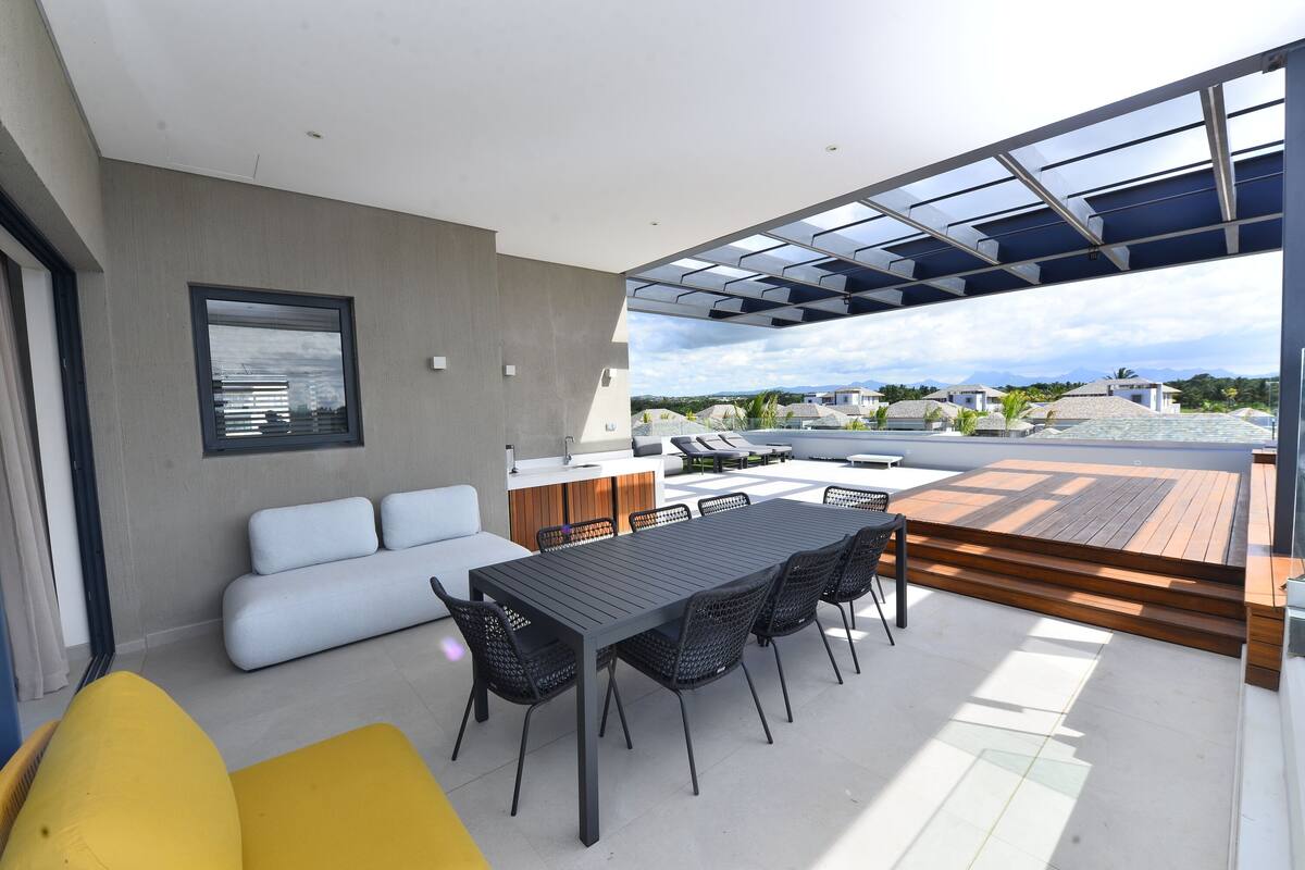 A modern outdoor patio with a dining table and chairs, a sofa, and a kitchen area with a countertop and sink.