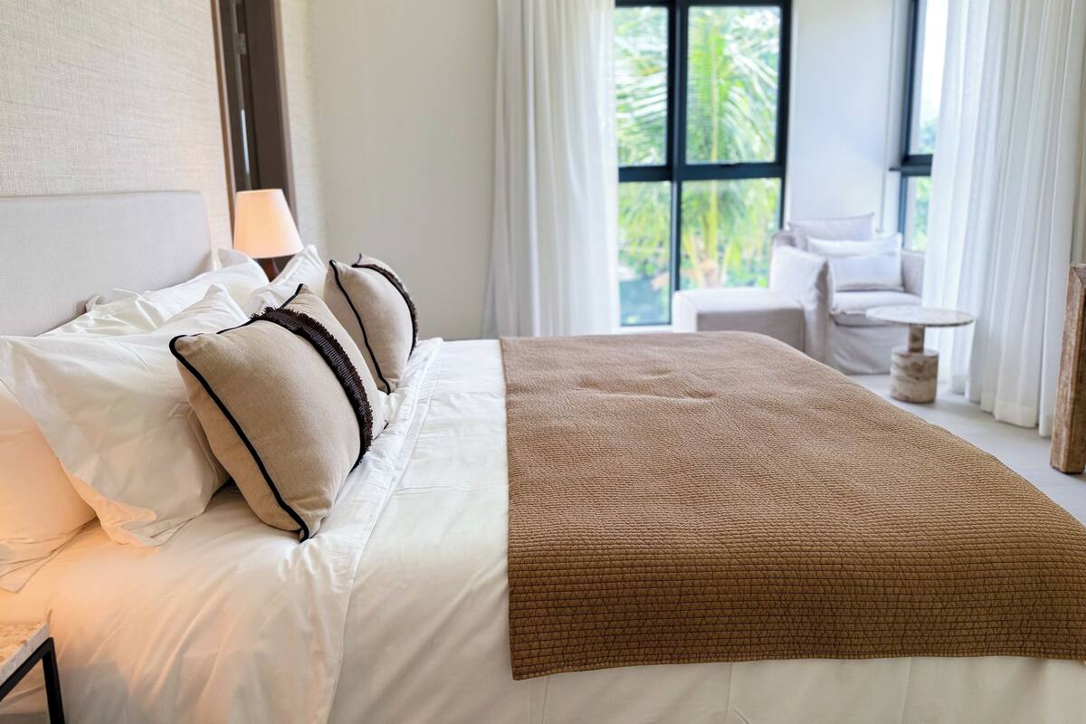 A hotel room with a large bed, a bedside lamp, and a view of the outdoors through a window.