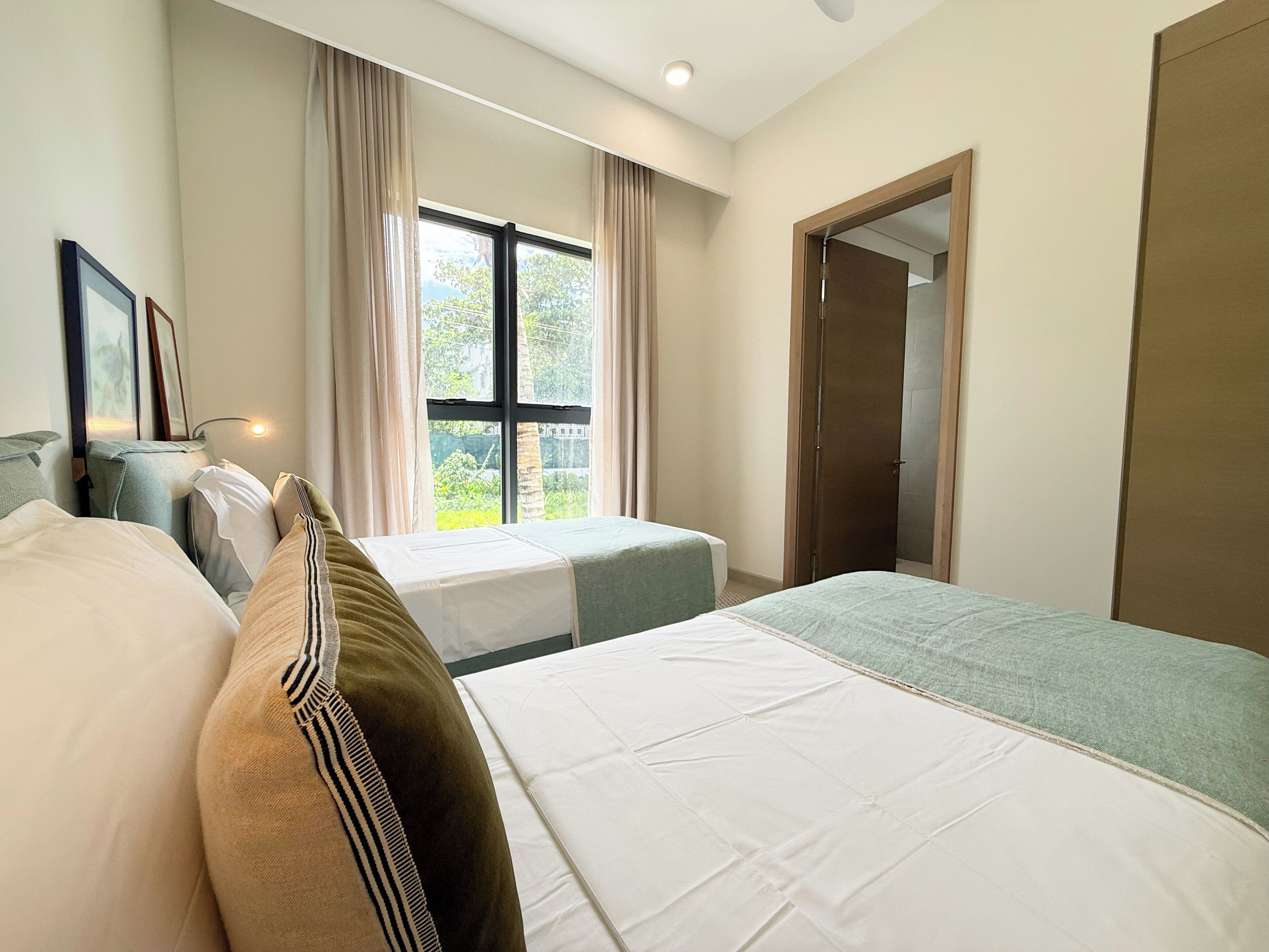 A hotel room with two beds, a large window with curtains, a door, and a framed picture on the wall.