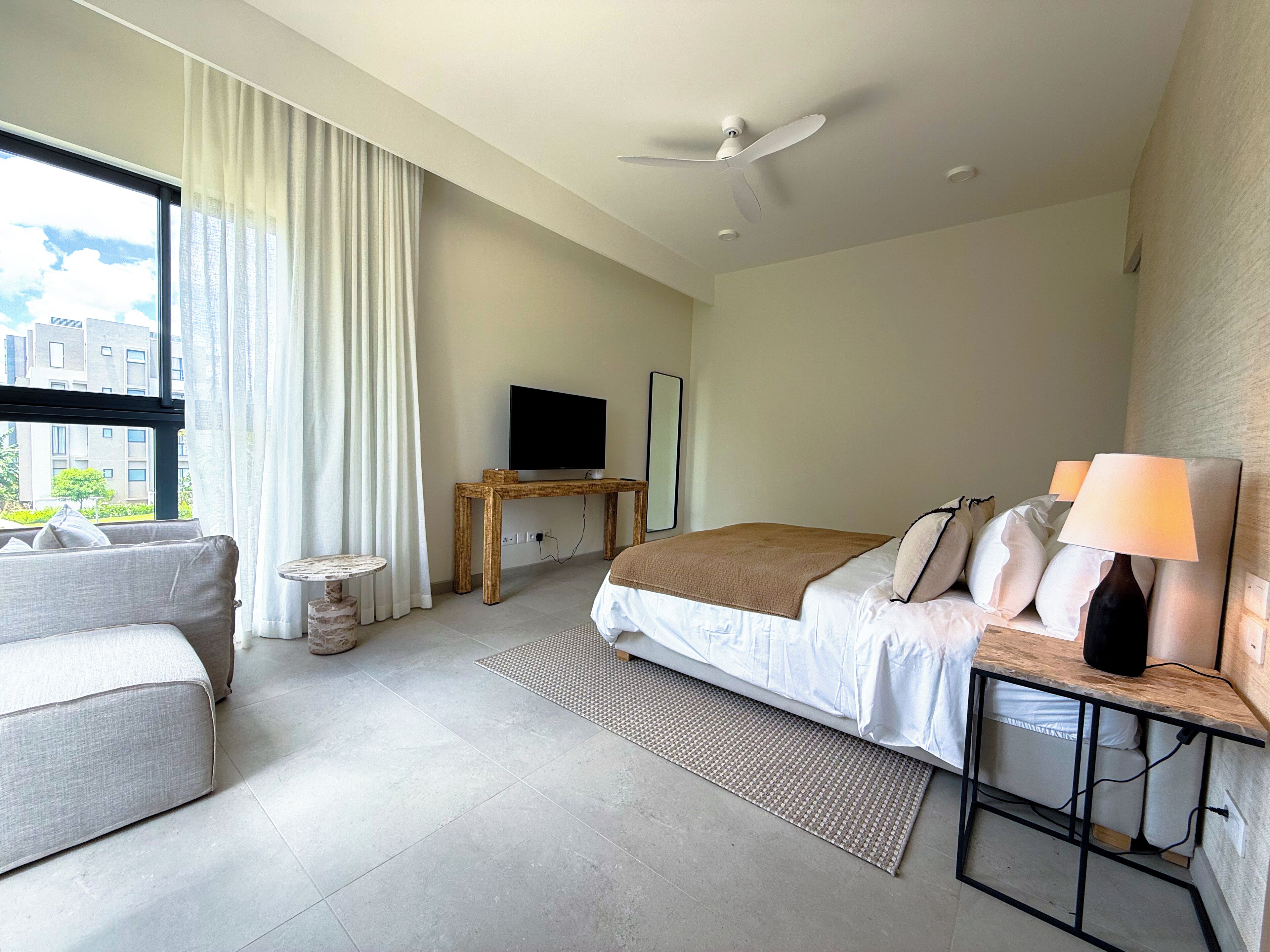 A modern hotel room with a bed, a TV, a desk, a chair, and a window with curtains.
