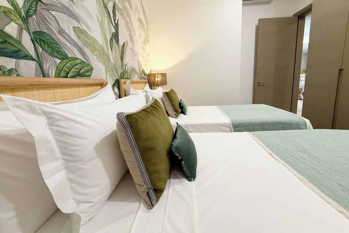 A hotel room with two beds, a large tropical mural on the wall, and a door leading to the outside.