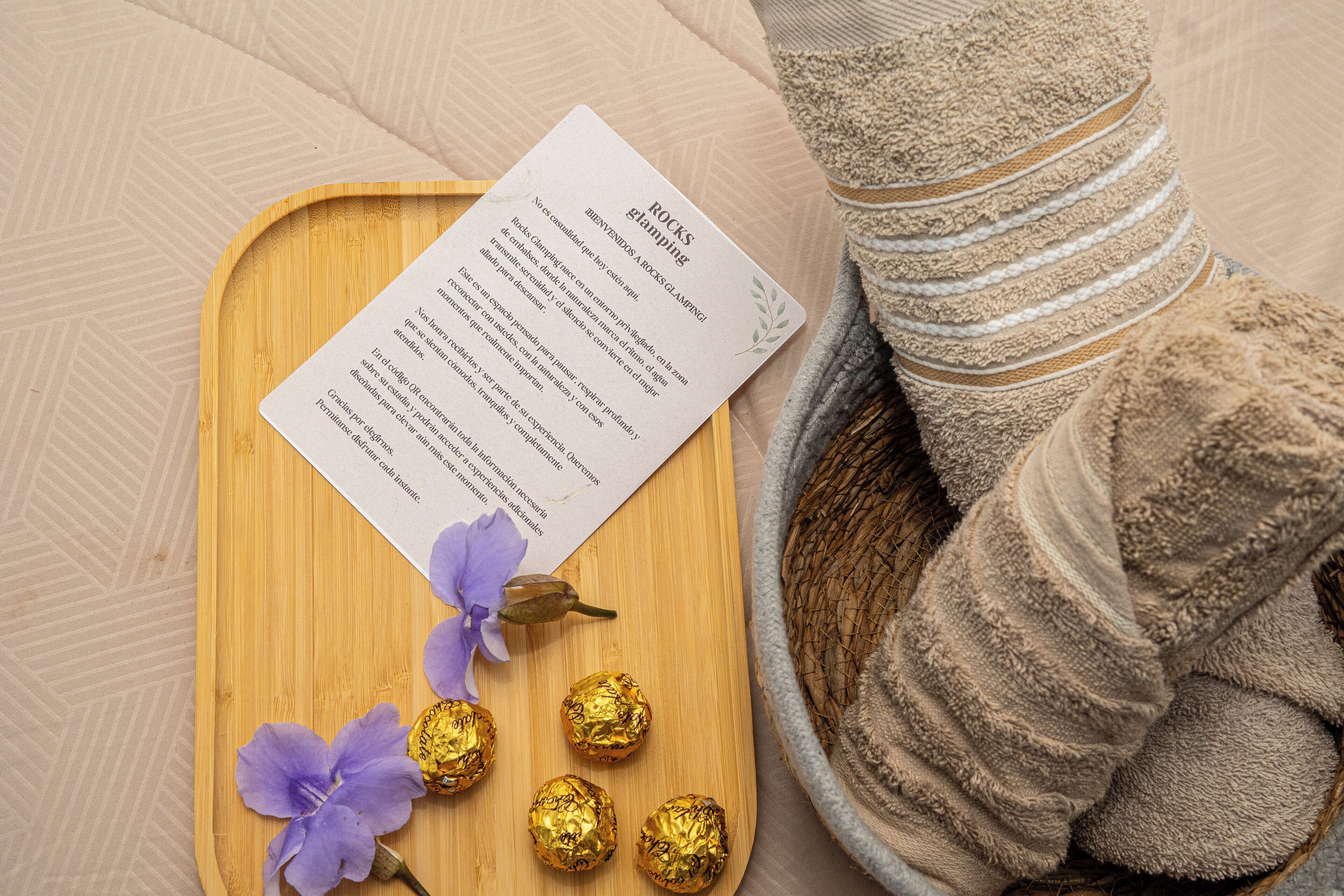 Een houten dienblad met een menukaart, een opgerolde handdoek en enkele ingepakte chocoladebonbons.