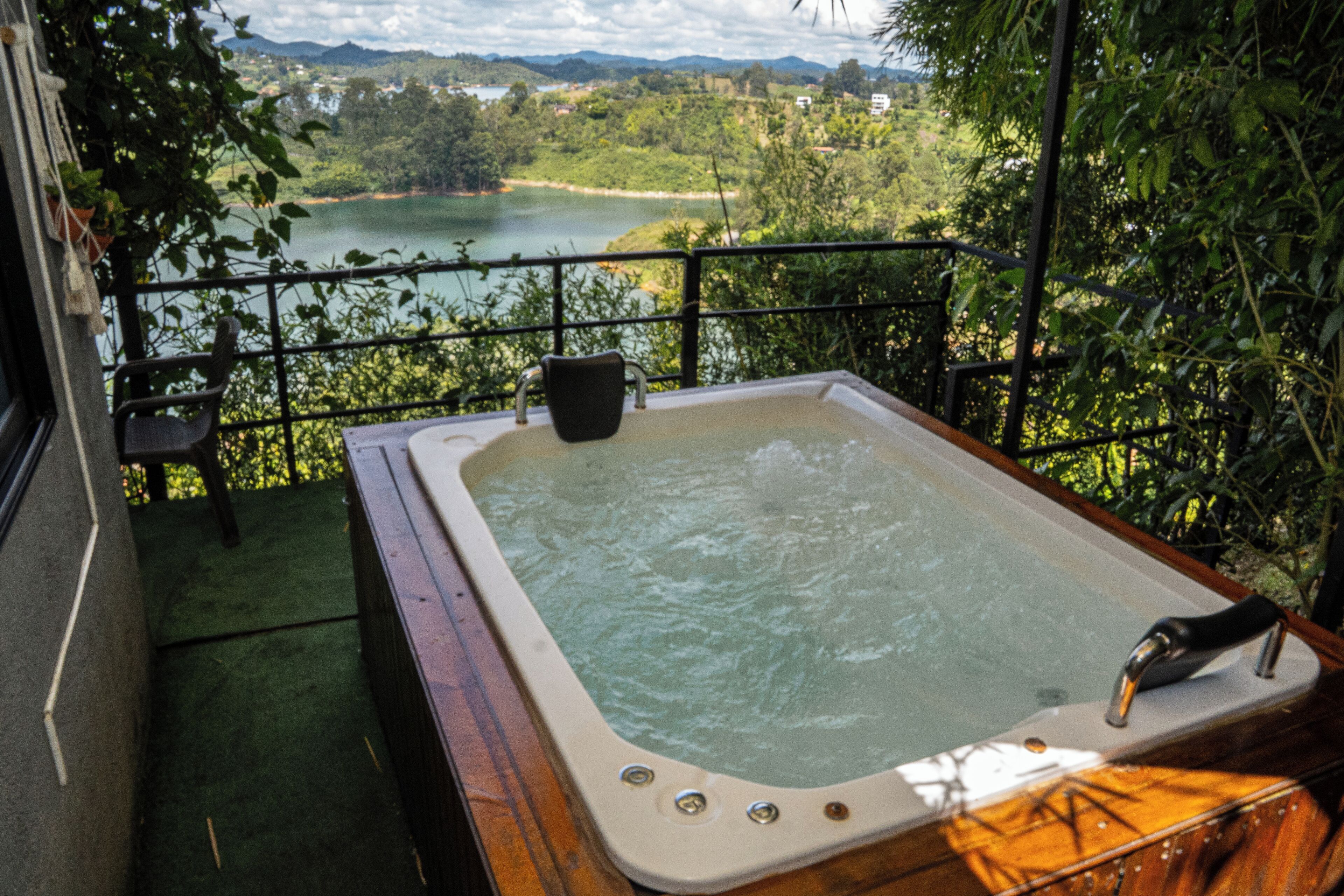 Un jacuzzi en un balcón con vista a un lago y follaje circundante.