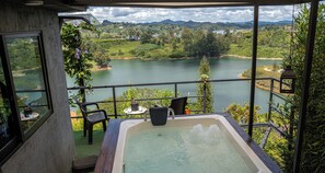 A balcony with a hot tub overlooking a lake, surrounded by greenery and mountains. - Rocks Glamping (El Peñol)