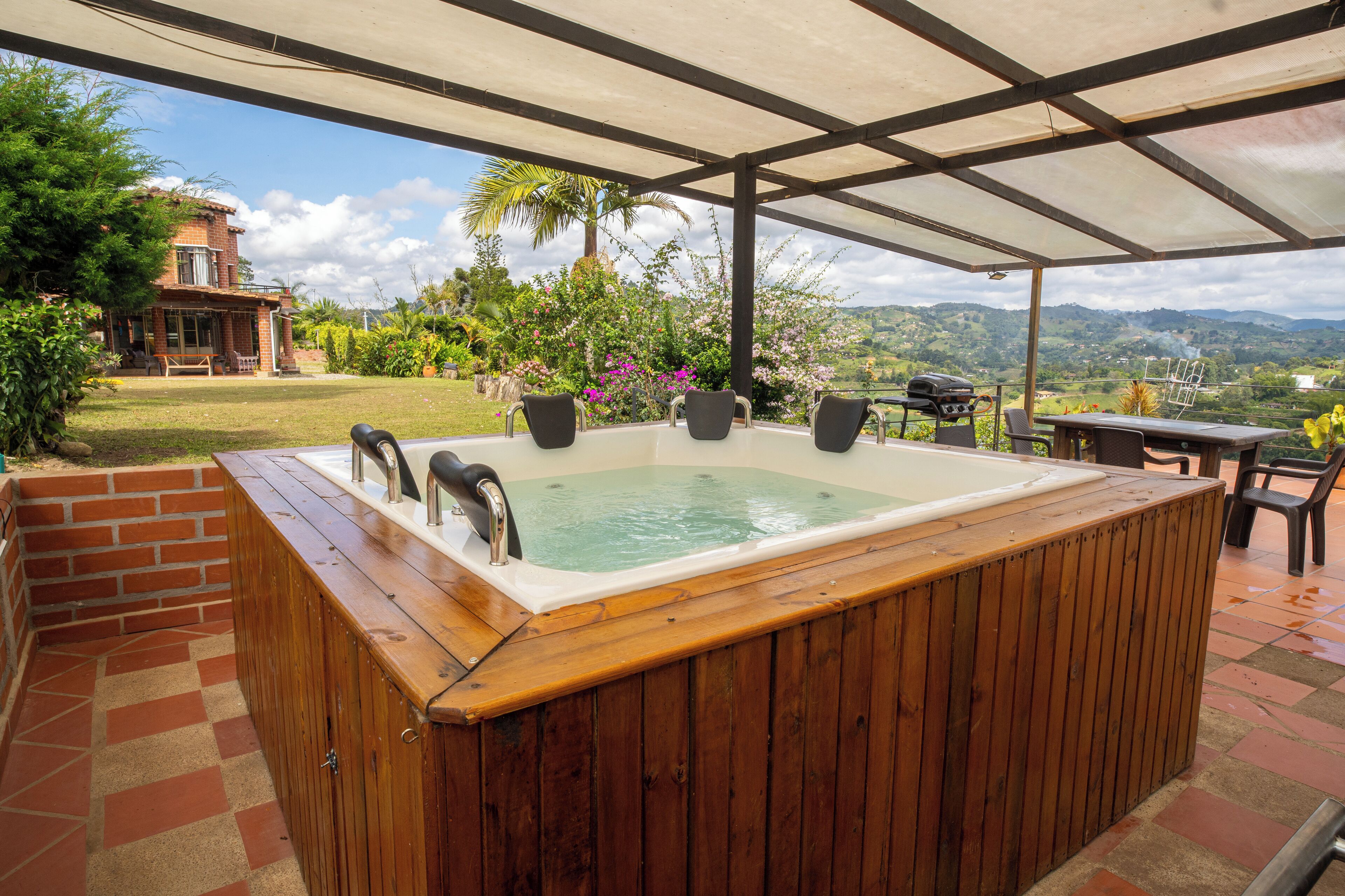 A wooden hot tub with a view of a house and mountains.