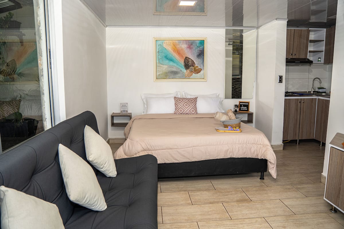 A modern bedroom with a bed, a sofa, and a small kitchenette.