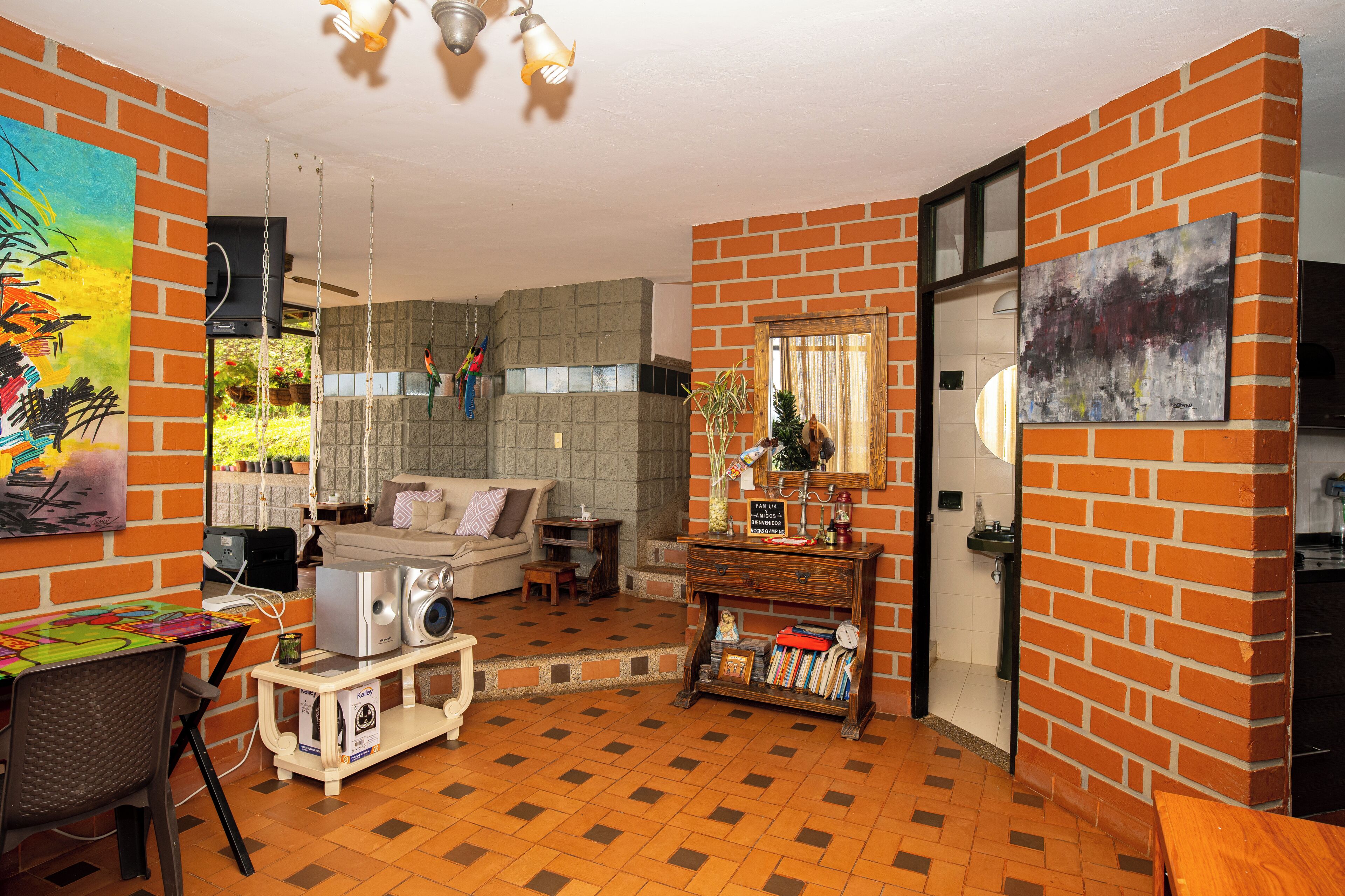 Un salon avec un mur en briques, un canapé, une table basse et un téléviseur. Une fenêtre offre une vue sur la verdure à l’extérieur.