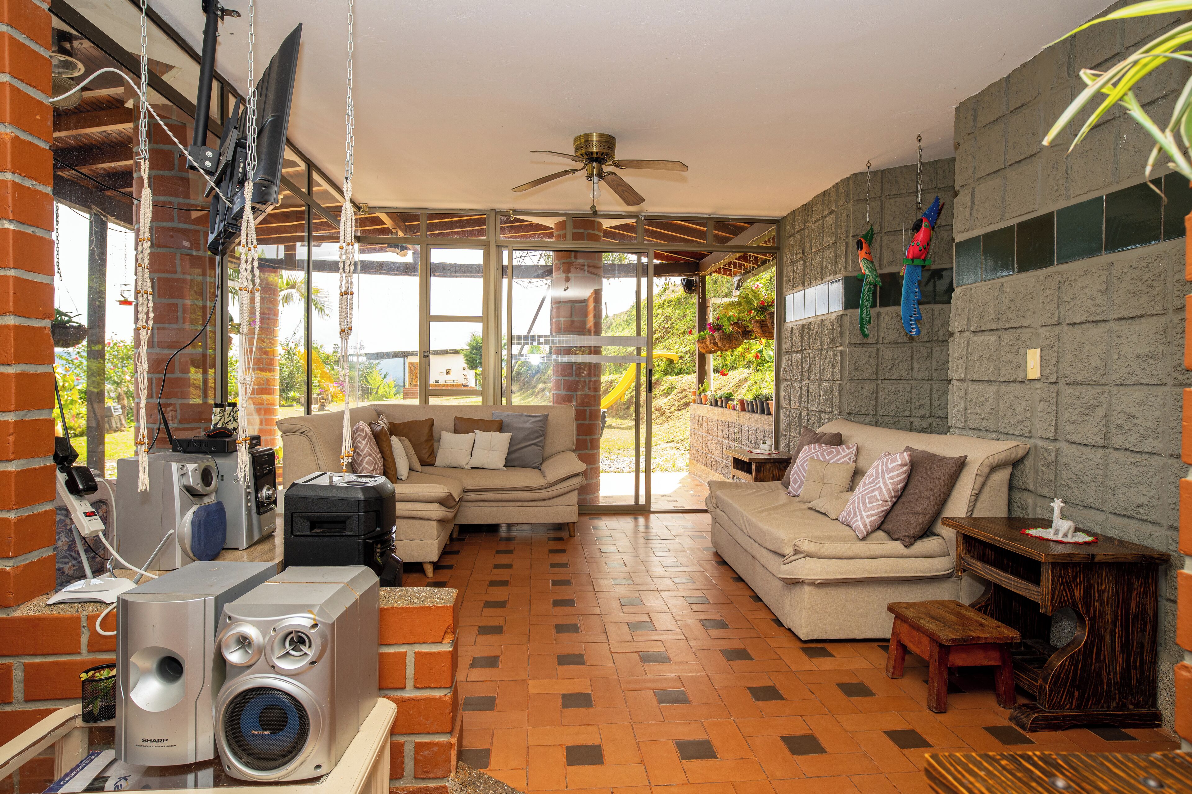 A spacious living area with a brick wall, a ceiling fan, and a large window overlooking a garden.
