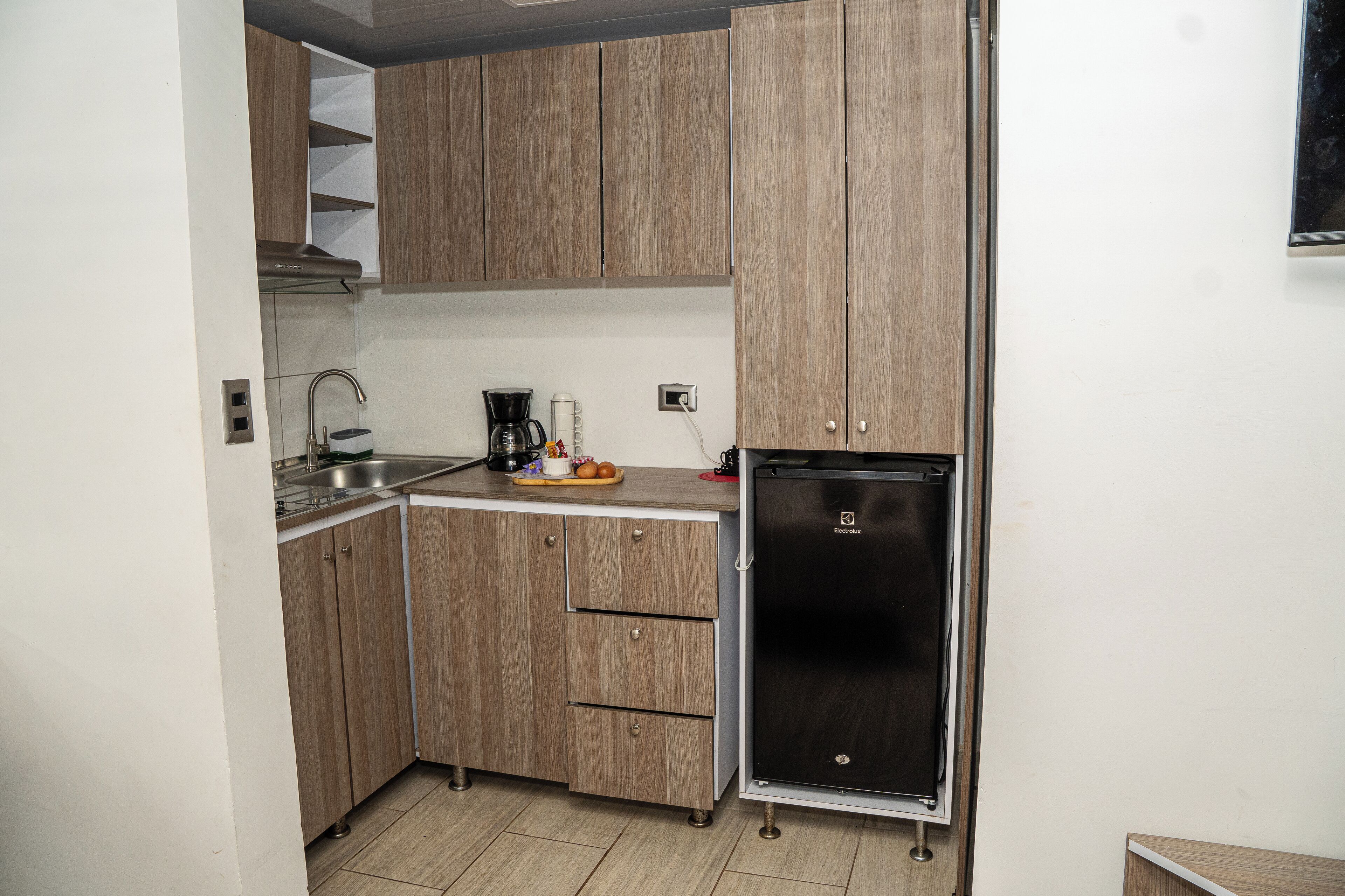 Une cuisine compacte avec des meubles en bois, un évier en acier inoxydable, une machine à café et un réfrigérateur noir.