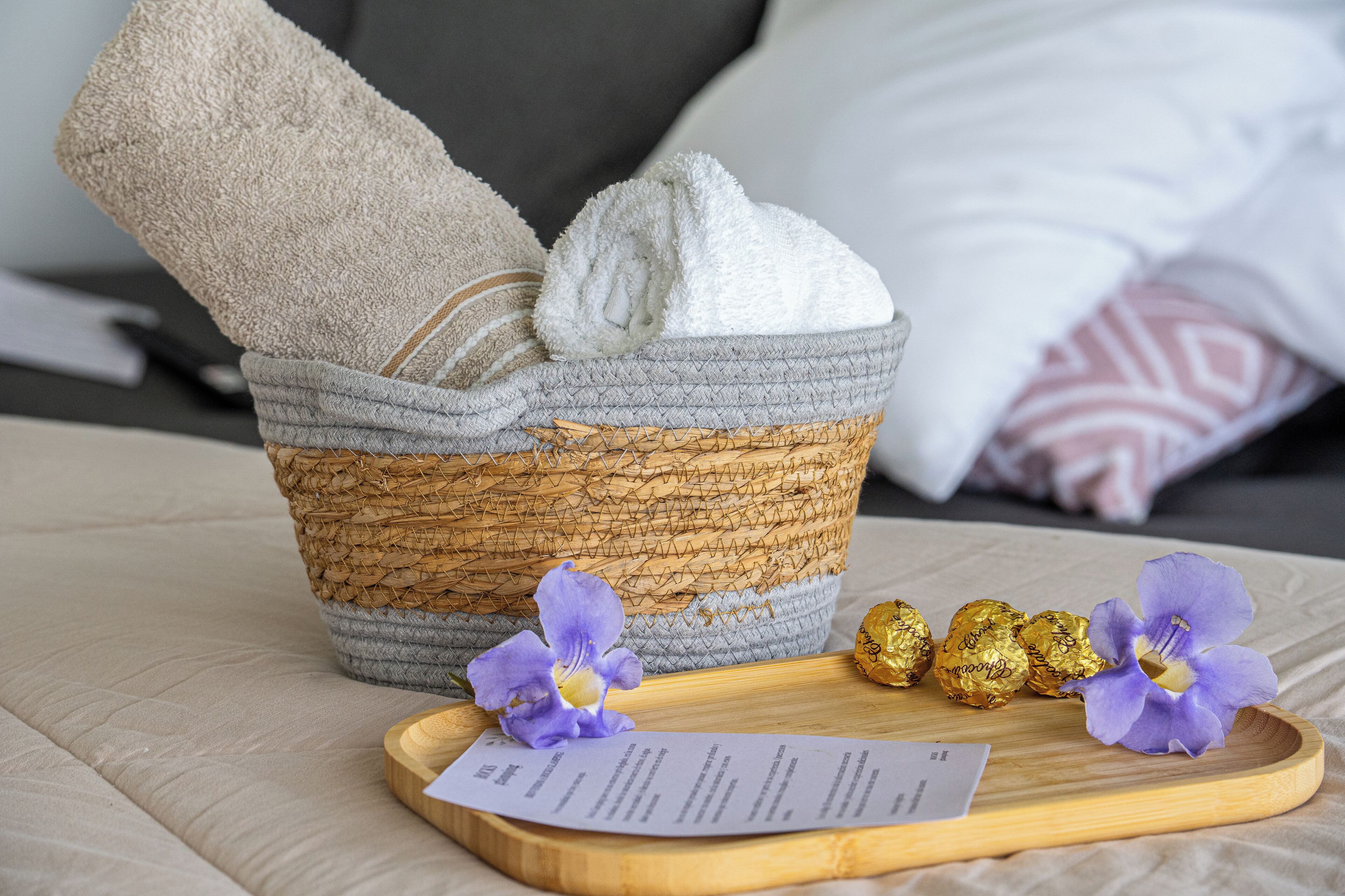 A basket with towels and chocolates on a tray, with a receipt on a cushion.